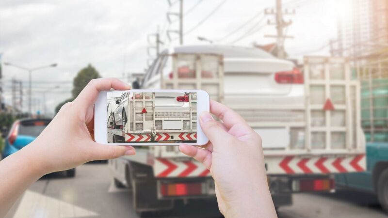 Using a smartphone to take a picture of a damaged car on a tow truck